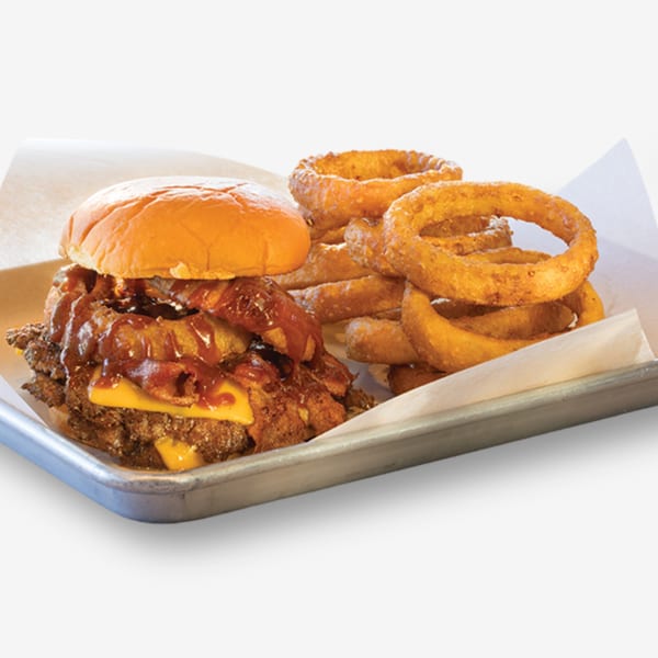 Cheeseburger with bacon, BBQ sauce, and onion rings on a metal tray with parchment paper.